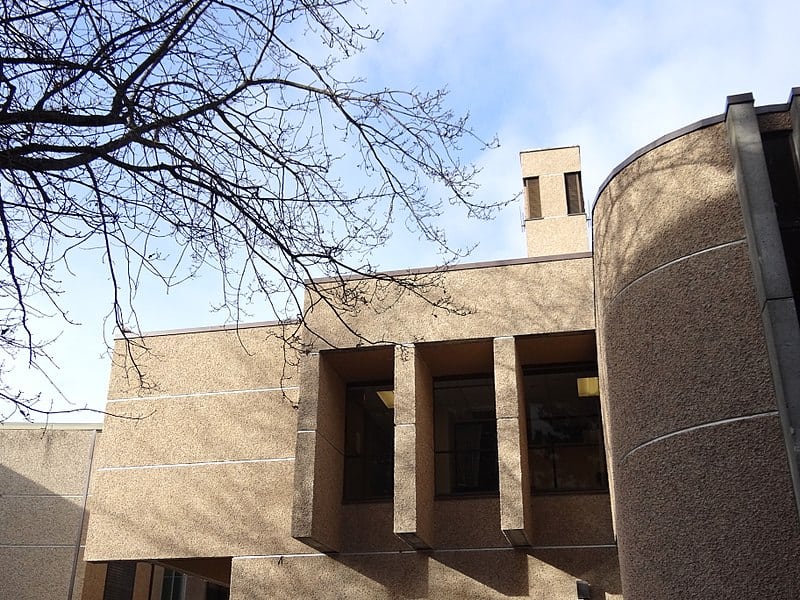Curved and angled concrete walls of a University of Victoria building, against a cloudy blue sky.