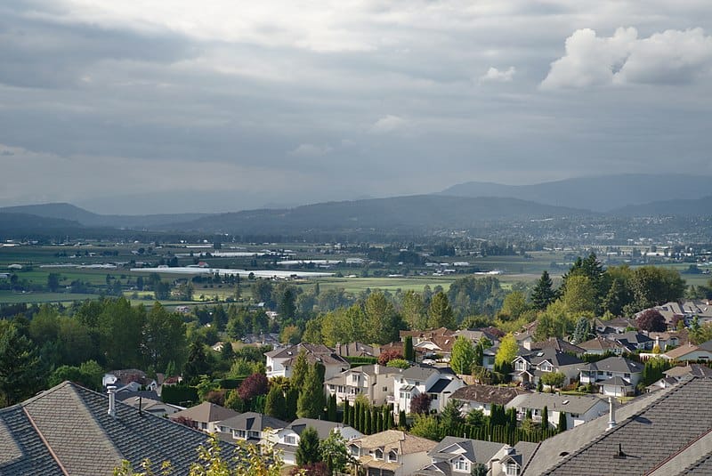 A view of Abbotsford, BC: cloudy skies, coastal mountains, green valley, somewhat-sprawling city.