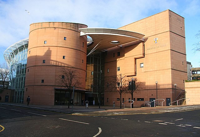 A postmodern red brick library building: two four-storey structures, one round, one rectangular, linked by a metal roof which evokes the bridge of the Starship Enterprise. (Abertay University Library, UK)