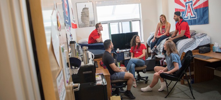 A group of students from the University of Arizona making the most of their dorm room’s space with a folding cushion chair.