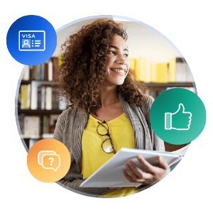 A photo of a female student, smiling, standing in a library holding an open book