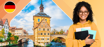 A young woman carrying a tablet and notebooks stands in front of a German canal with a tower at its centre.